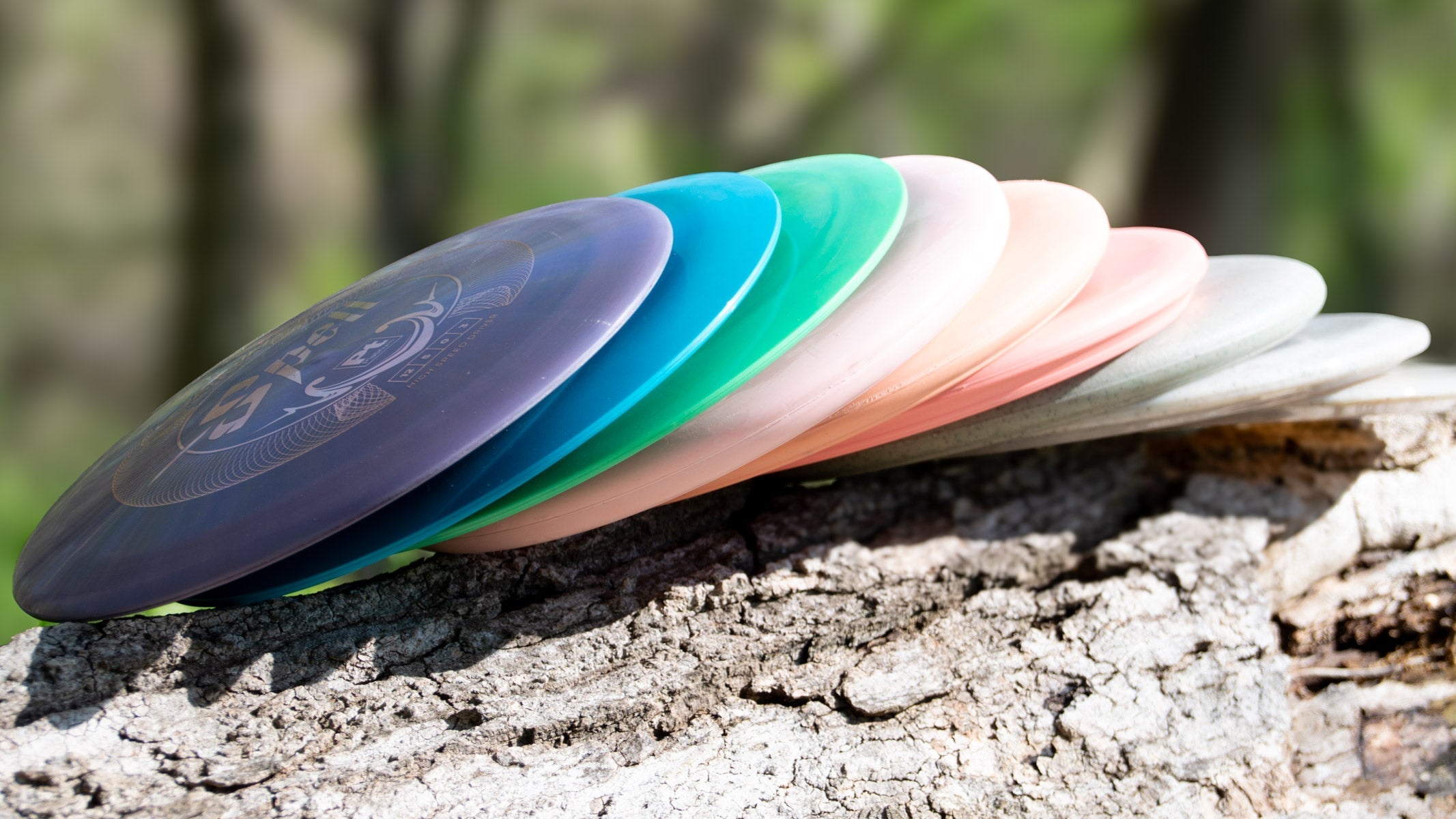A stack of colorful disc golf discs rests on a tree trunk outdoors with a blurred green background.
