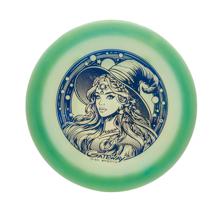 The Spell NXT Superglow - PremierJul is a glow plastic disc golf driver with a green rim, featuring a central witch hat woman illustration surrounded by stars and "Gateway Disc Sports" below.