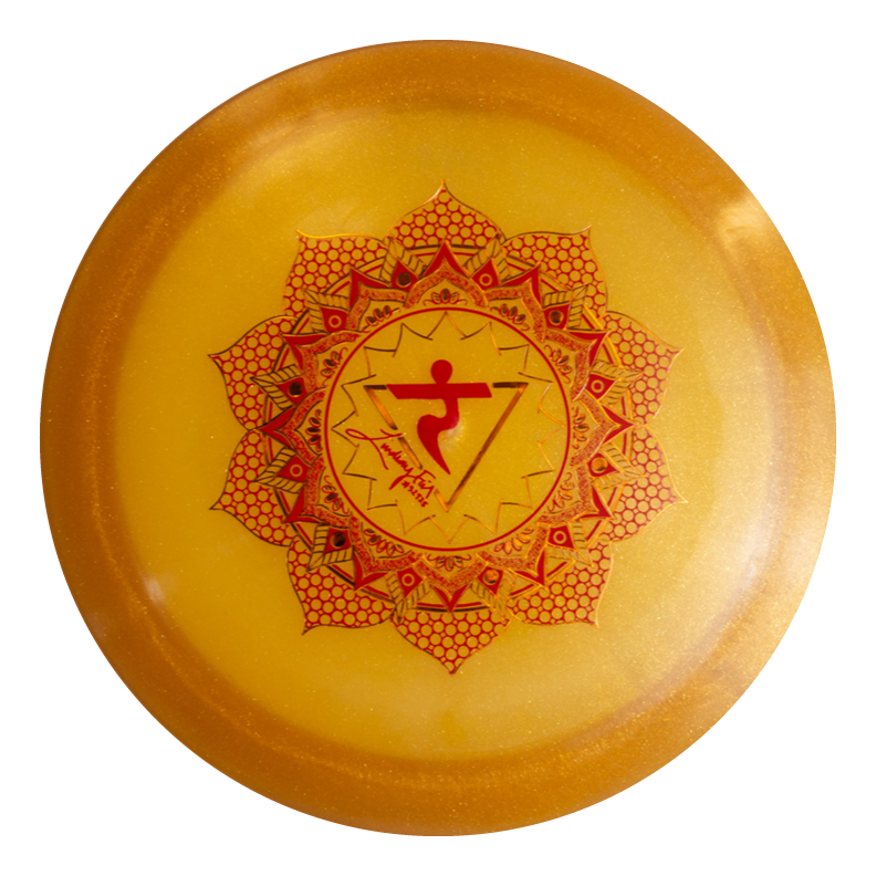 The Lindsay Fish's Assassin - Diamond Metal Flake is a round yellow disc with a red mandala and central symbol, perfect for disc golf fairway drives and inspired by the solar plexus chakra.