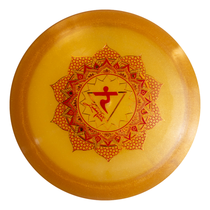 The Lindsay Fish's Assassin - Diamond Metal Flake is a round yellow disc with a red mandala and central symbol, perfect for disc golf fairway drives and inspired by the solar plexus chakra.