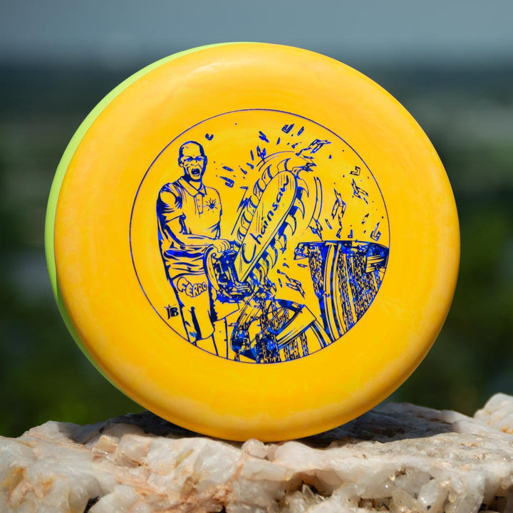 A yellow Black Zombie Chainsaw — SS disc from BZ Sports, featuring a blue man and basket illustration, rests on a rock outdoors. This stable putter is ideal for precision shots.