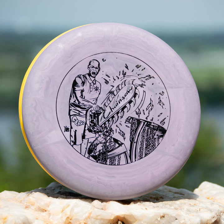 A lavender Black Zombie Chainsaw — SS stable putter featuring black line art of a disc thrower and "Chainsaw" text, shown outdoors on light stone.