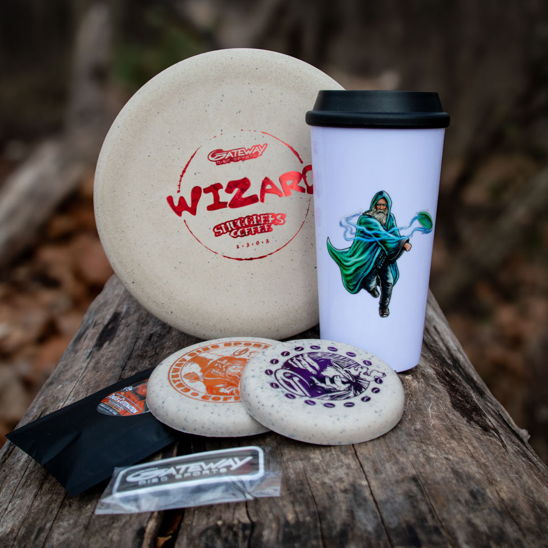 Grab the limited-time Coffee Wizard & Mug Set: three disc golf discs, a Smugglar's Coffee Wizard travel mug, sticker, and pouch€”all arranged on a wooden surface outdoors. Don't miss out!.
