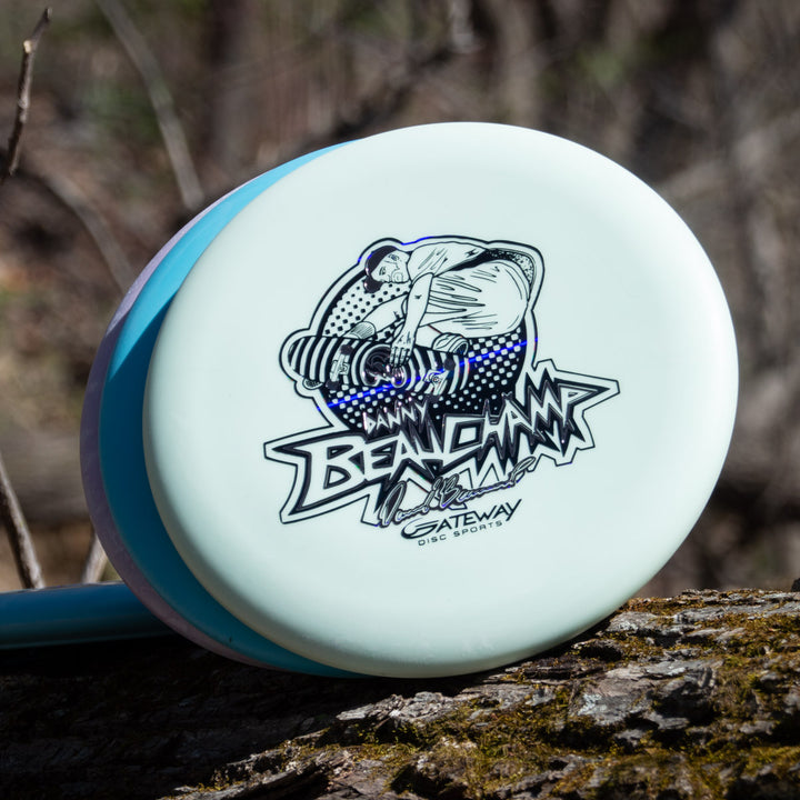 Danny Beauchamp's Signature Retro Wizard - SS - Superglow putter, with a black and white thrower illustration and "Danny Beauchamp Gateway Disc Sports" text, sits on a log outdoors, highlighting the Gateway lineup.