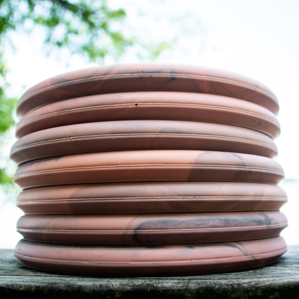 A stack of ten pink and black marbled Devilhawk - SureGrip™ Eraser discs, known for excellent grip, sits outdoors on a wooden surface.