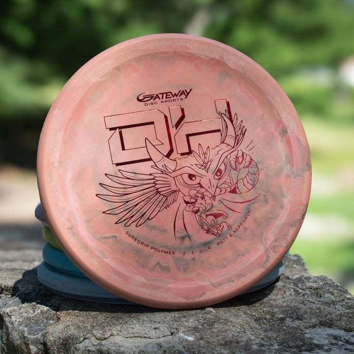 A pink Devilhawk - SureGrip™ Swirly Special Edition putter featuring an owl illustration stands upright on a stone surface outdoors.