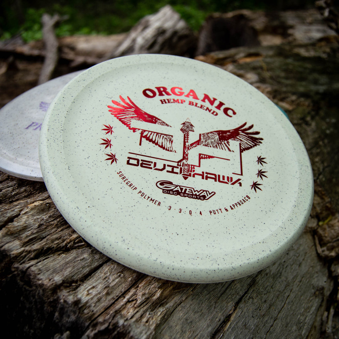 A white overstable Devilhawk - Suregrip Hemp putter by Gateway Disc Sports featuring a Thumb Track design is displayed on a wooden surface outdoors.