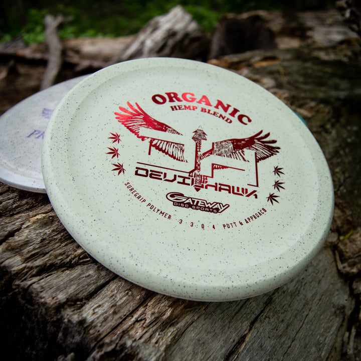A white overstable Devilhawk - Suregrip Hemp putter by Gateway Disc Sports featuring a Thumb Track design is displayed on a wooden surface outdoors.