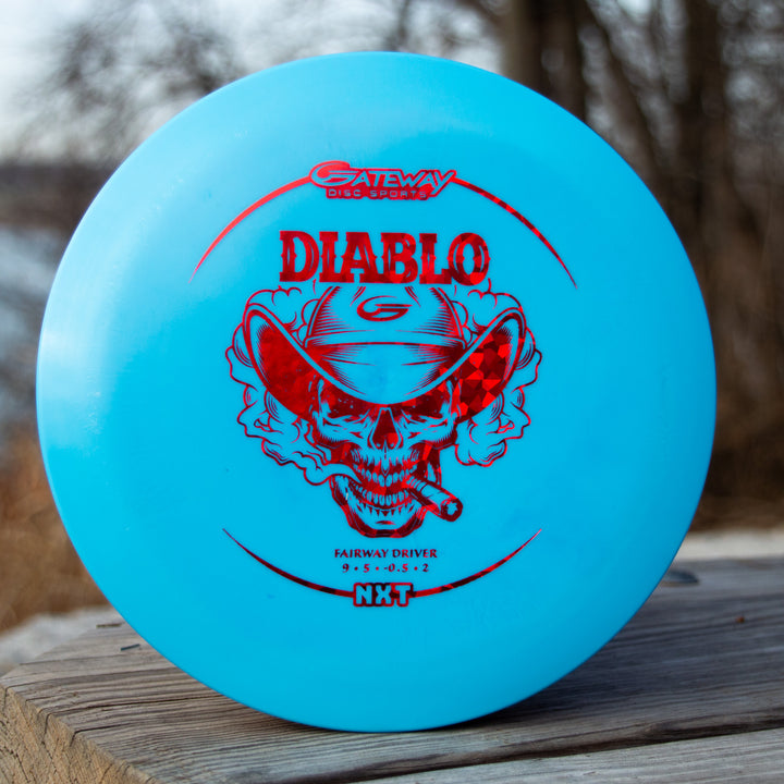 A blue Diablo - NXT overstable fairway driver disc, featuring a red skull in a cowboy hat and bandana graphic, displayed outdoors on wood—ideal for distance flex shots and precise landings.