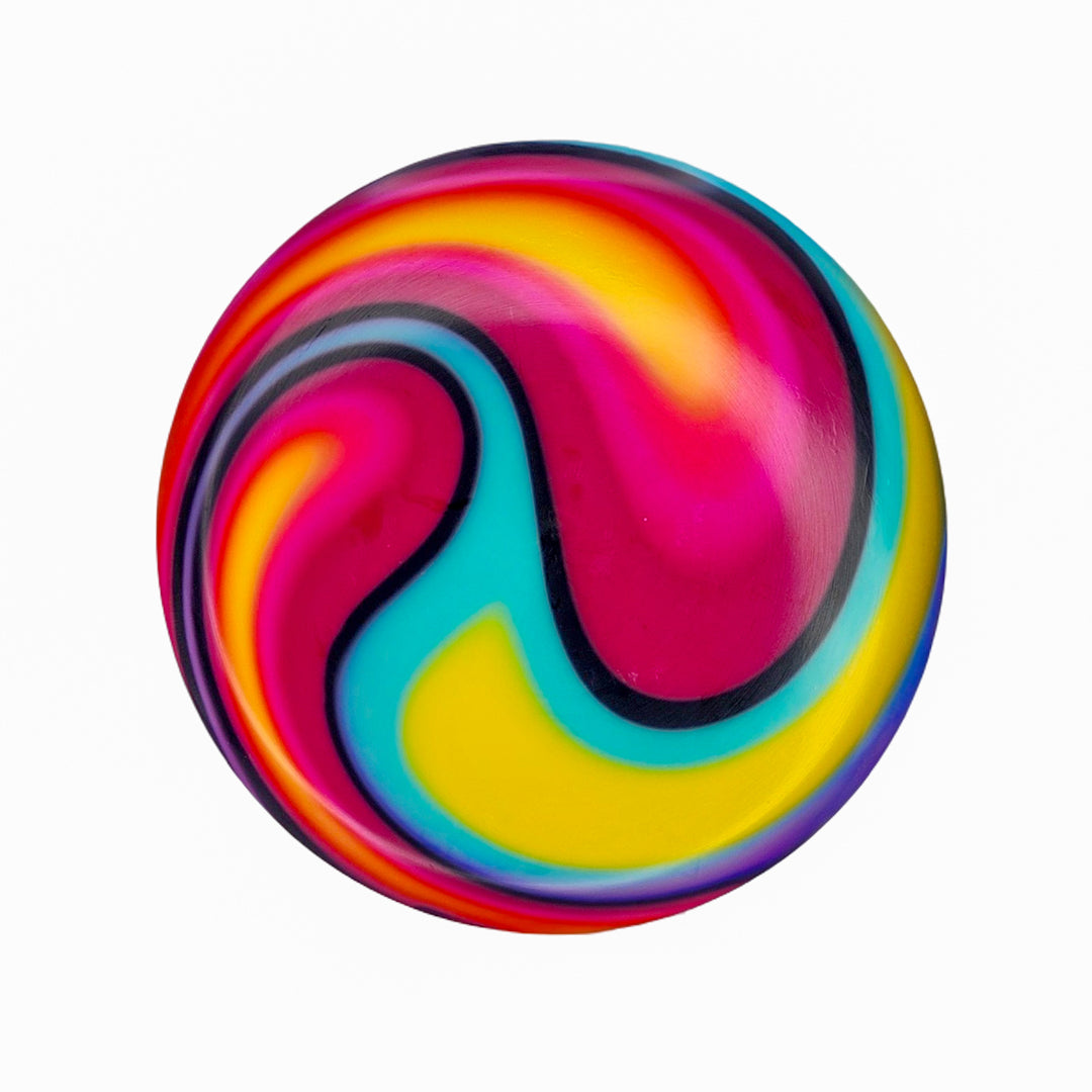 The Element - NXT - Optic Dyes features a round shape with a vibrant swirl pattern in yellow, pink, blue, red, and black on white, reminiscent of hand-dyed discs.
