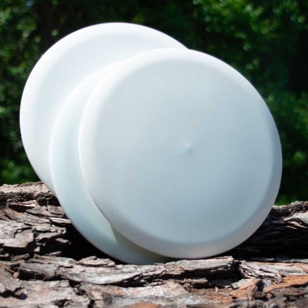 Two stacked Dye Canvas Element - NXT discs by Gateway Disc Sports rest on rough tree bark, with blurred green foliage in the background.