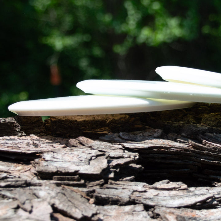 Three Dye Canvas Element - NXT discs from Gateway Disc Sports rest on a textured tree trunk outdoors, with blurred green foliage in the background.