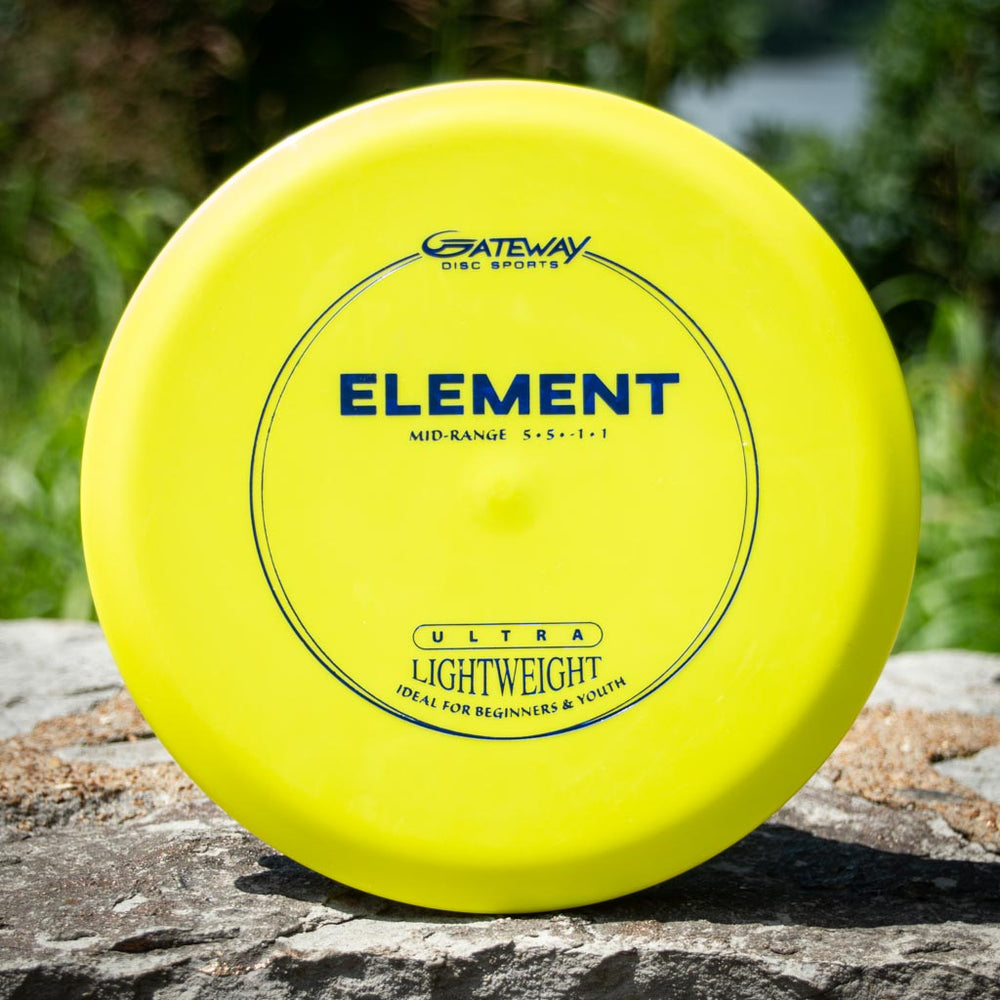 A yellow Element Ultra Lightweight - SureGrip™ mid-range disc golf disc sits on a rock, offering exceptional glide and straight flight, with lush greenery in the background.