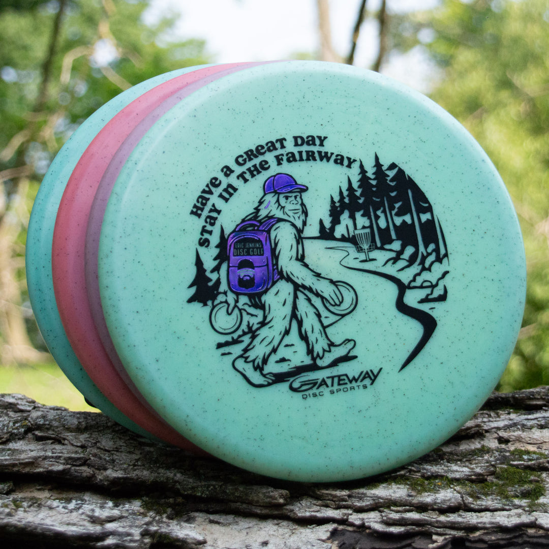 Three disc golf discs are stacked on a log. The top disc is the Eric Jenkins Signature Series Chief - Diamond Hemp, a low profile putter featuring a cartoon yeti and the text, —Have a Great Day, Stay in the Fairway. Gateway Disc Sports.—�.