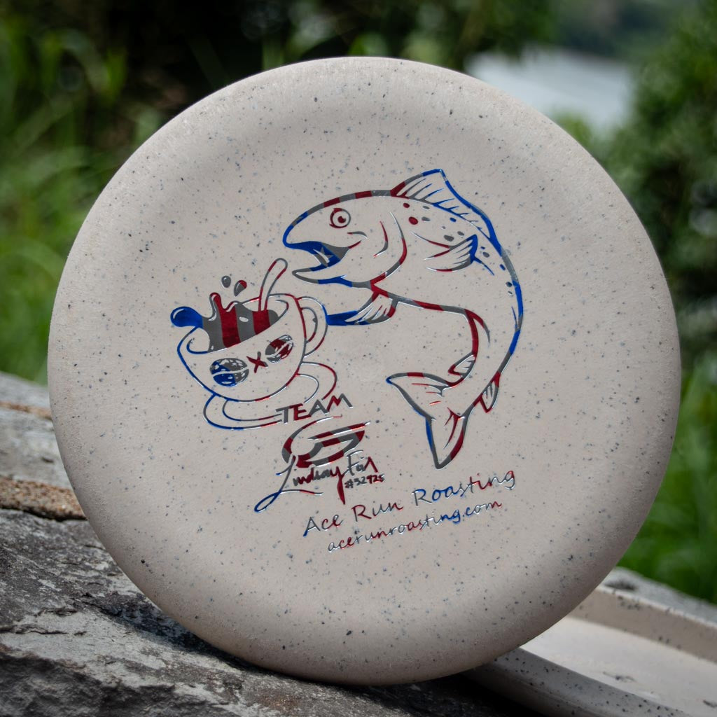 The Lindsay Fish Warlock - Coffee Blend features blue and red artwork of a coffee cup with arms and legs next to a jumping fish, labeled "Team Ace Run Roasting." Proceeds support Lindsay Fish.