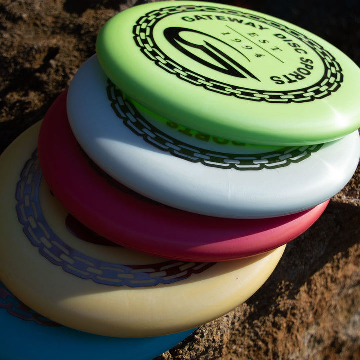 A stack of five colorful disc golf discs, including the iconic Wizard - Evolution - Frosty with a "Gateway Disc Sports" logo, placed on a rock outdoors.