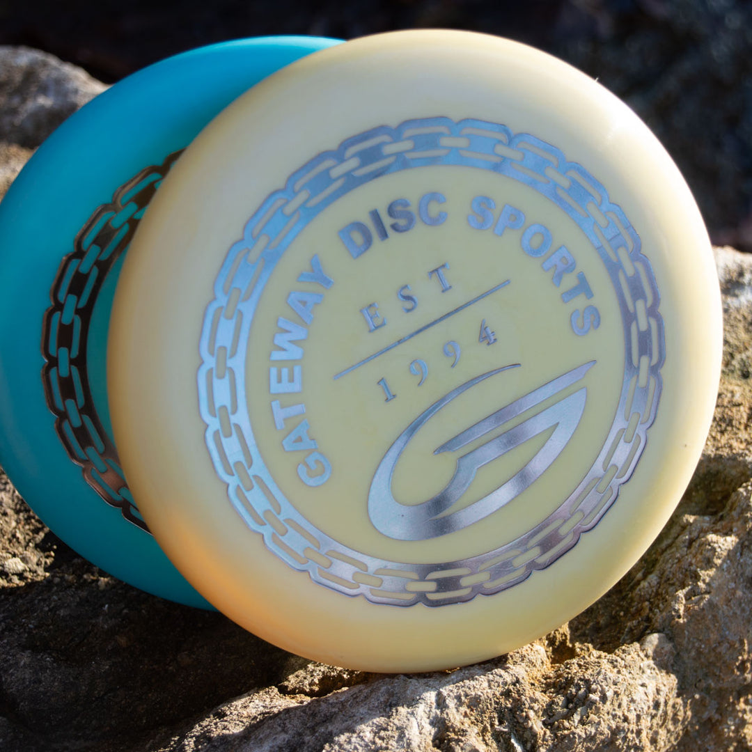 Two plastic discs rest on rocks, the front showing "GATEWAY DISC SPORTS EST 1994" with a chain graphic, featuring the Wizard - Evolution - Frosty disc.