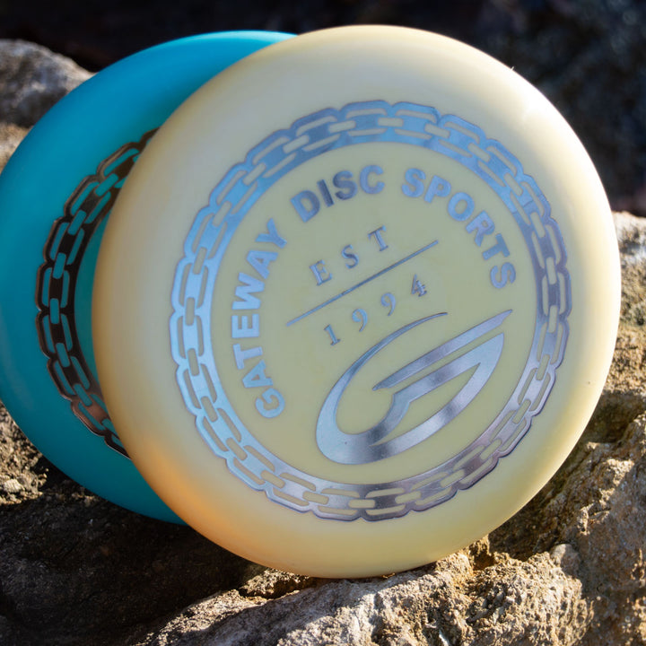 Two plastic discs rest on rocks, the front showing "GATEWAY DISC SPORTS EST 1994" with a chain graphic, featuring the Wizard - Evolution - Frosty disc.