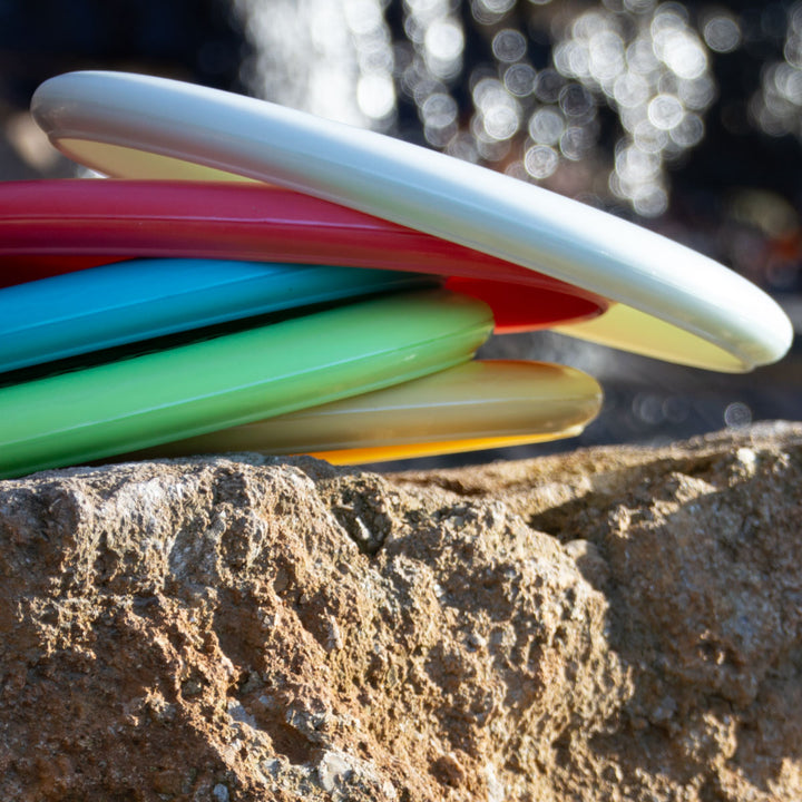 A stack of colorful frisbees, featuring the Wizard - Evolution - Frosty disc, rests on a rugged outdoor rock.
