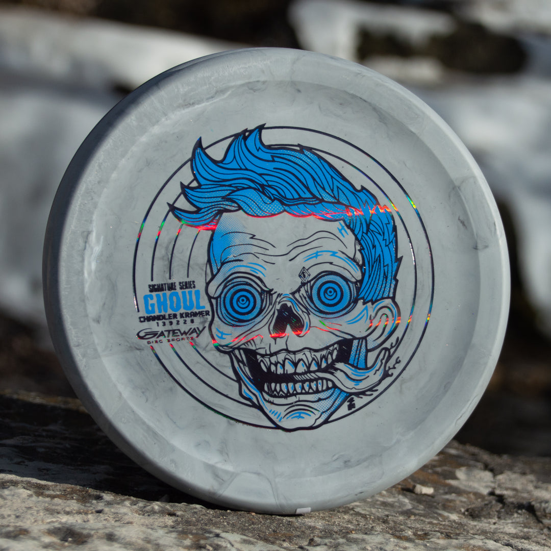 A gray disc golf disc called "Chandler's Special Edition Ghoul - Lunar" features a zombie face with blue hair, perfect for power throwers seeking a stable overstable approach disc with comfortable forehand grip.