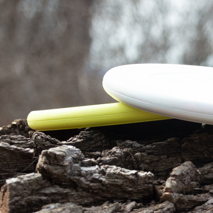 Close-up of two Ghoul - Chandler Kramer Signature Series discs, one yellow and one white, resting on rough tree bark with a blurred natural background—ideal for disc golfers wanting stable approach shots and reliable flights.