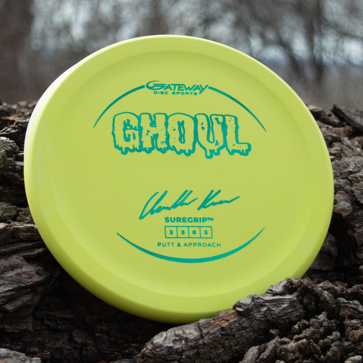 A yellow Ghoul - Chandler Kramer Signature Series disc from Gateway Disc Sports rests on rough tree bark outdoors, poised to deliver reliable flight and control for your next approach shot.