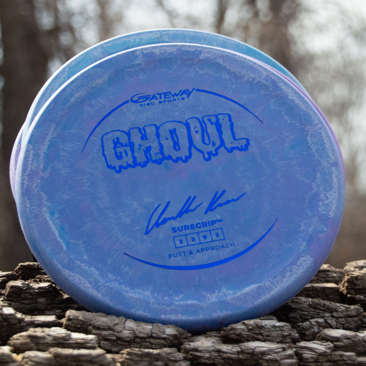 A blue Ghoul - Chandler Kramer Signature Series disc by Gateway Disc Sports with "SureGrip" and "Putt & Approach" text, pictured on textured wood outdoors—perfect for players seeking reliable flight in a stable approach disc.