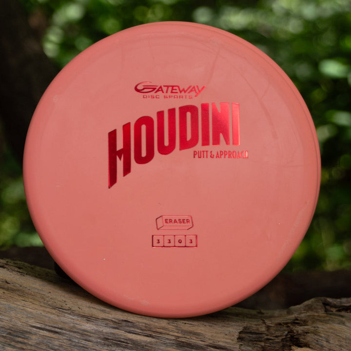A pink Houdini - Eraser putt and approach disc by Gateway Disc Sports, ideal for power-gripping backhands, rests on wood with a blurred green background.