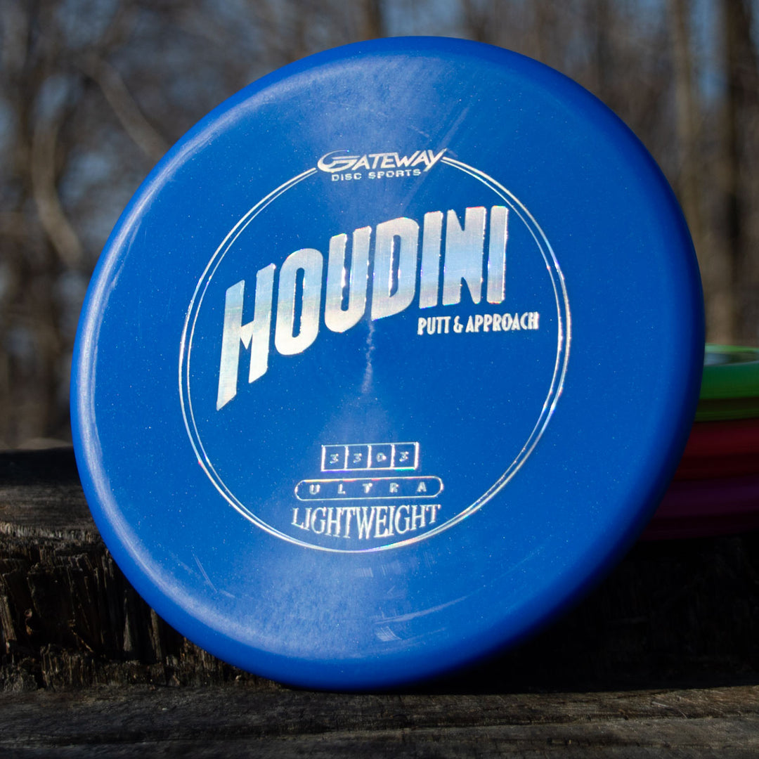 A blue Houdini - SureGrip™ Ultra Lightweight putt & approach disc rests on a wooden surface outdoors.
