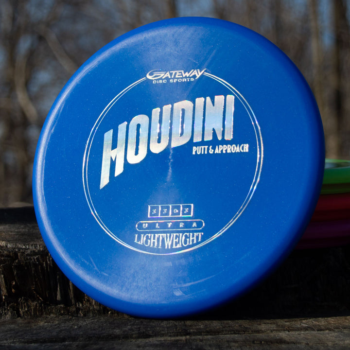 A blue Houdini - SureGrip™ Ultra Lightweight putt & approach disc rests on a wooden surface outdoors.