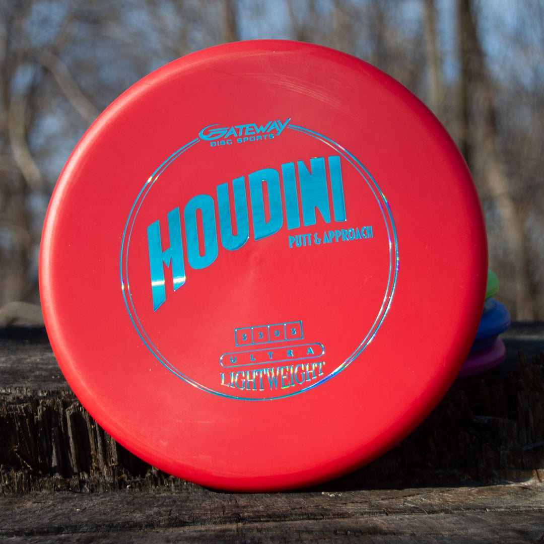 A Houdini - SureGrip™ Ultra Lightweight putt and approach disc in red with blue text and a deep rim rests on a wooden surface outdoors.