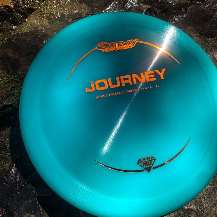 A blue Journey - Hyper Diamond (HD) disc golf driver, recognized for its controllable flight as a —Stable Distance Driver,—� sits on a sunlit rock surface.
