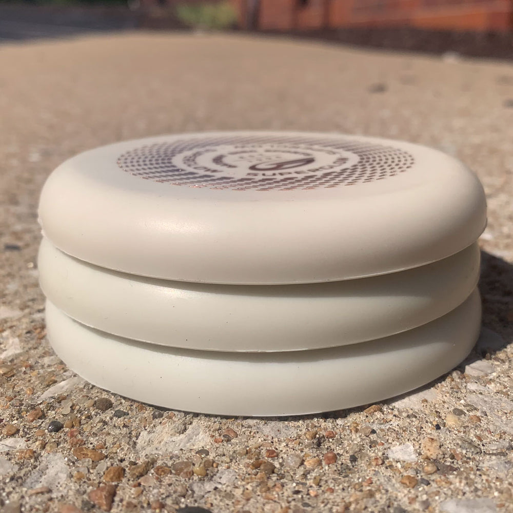 Three Mini (Large) - Superglow white flying discs are stacked on a concrete surface, featuring a circular patterned design on the top disc.