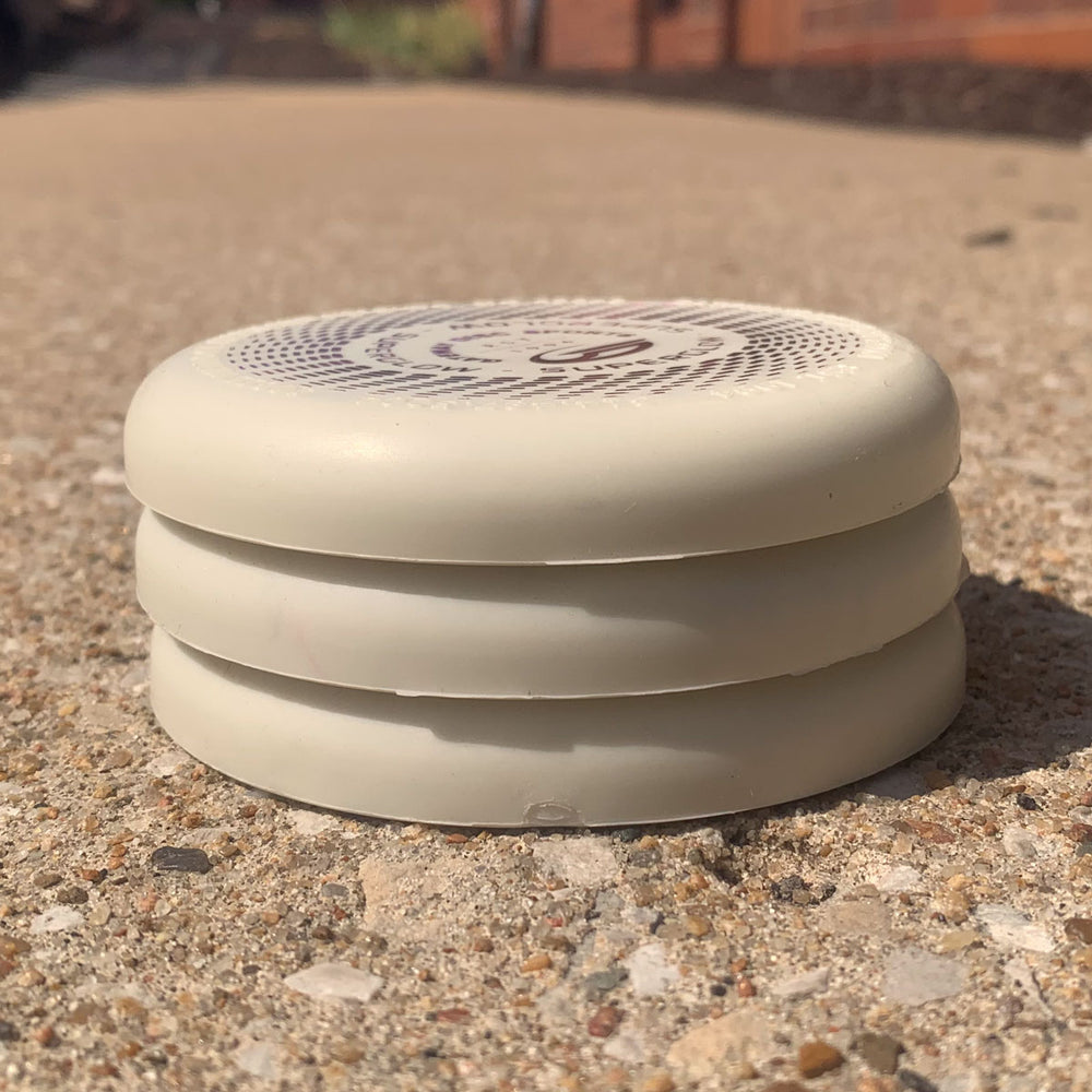 A white, round, vented Mini (Small) — Superglow with three stacked layers rests on a textured outdoor surface in sunlight.