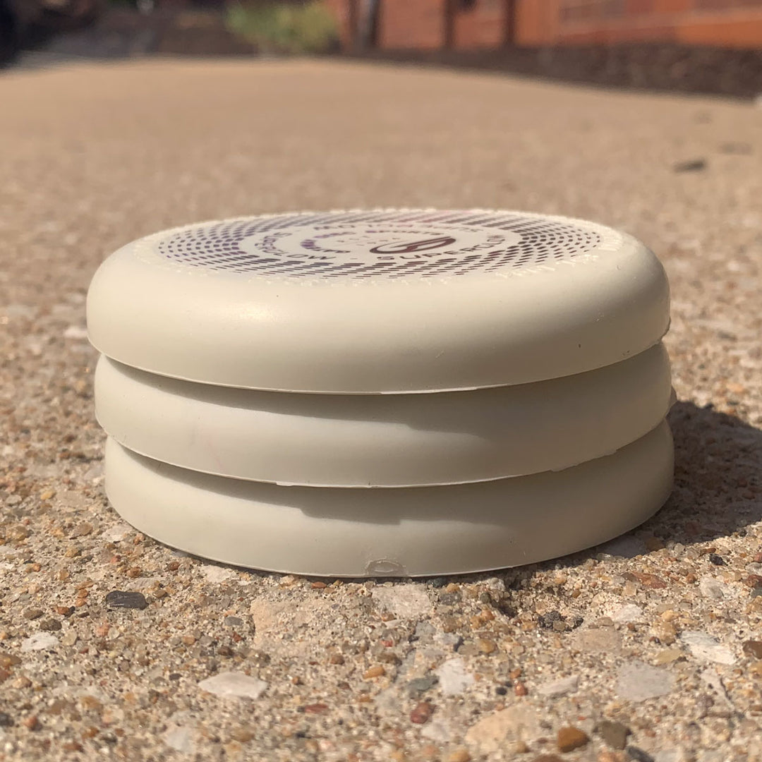 A white, round, vented Mini (Small) — Superglow with three stacked layers rests on a textured outdoor surface in sunlight.