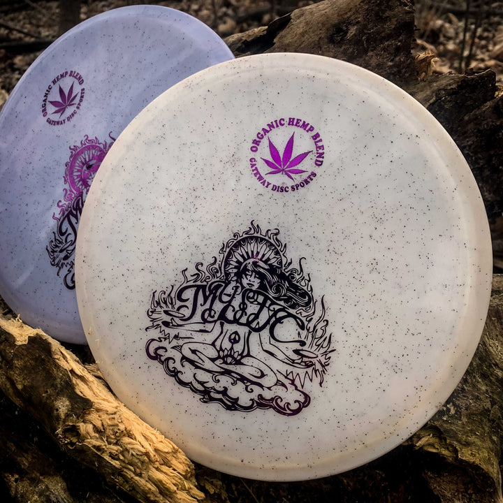 Two Mystic - Diamond Hemp disc golf discs rest on a log; both have speckled surfaces, detailed designs, and —Organic Hemp Blend—� text with a cannabis leaf, ideal for players wanting reliable straight mid-range throws.