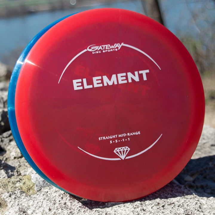 A red Element - Diamond mid-range disc golf disc by Gateway Disc Sports, featuring flight numbers 5, 5, -1, 1 and known for its glide and straight flight, rests on a rock outdoors.