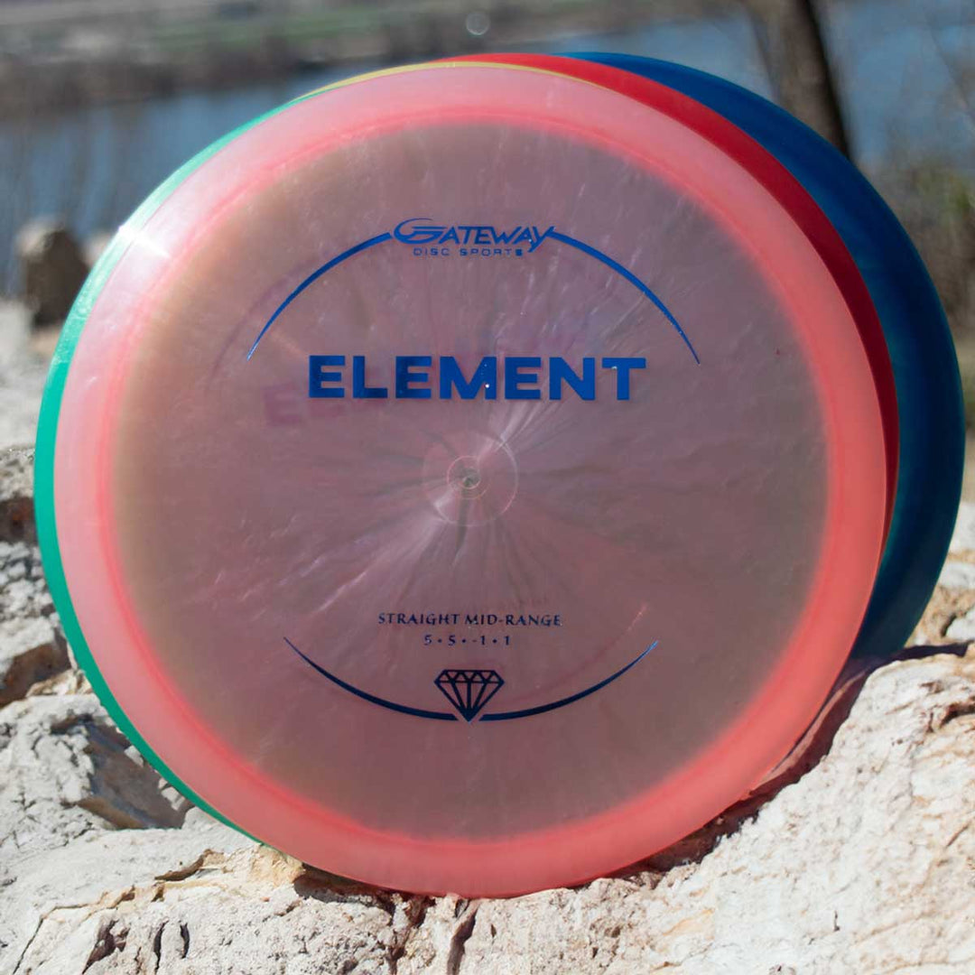 A Gateway Element - Diamond mid-range disc with a transparent pink rim and blue lettering rests on a rock outdoors, known for its straight flight and excellent glide.