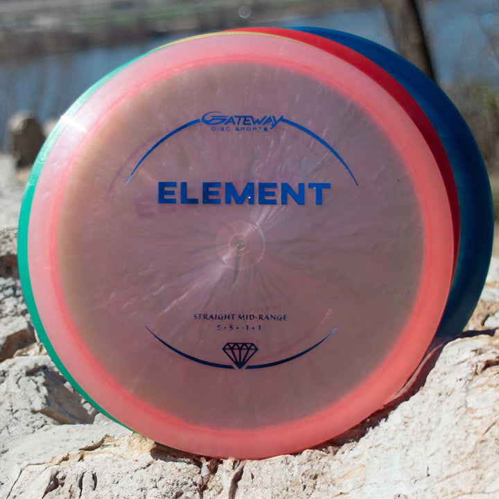 A Gateway Element - Diamond mid-range disc with a transparent pink rim and blue lettering rests on a rock outdoors, known for its straight flight and excellent glide.
