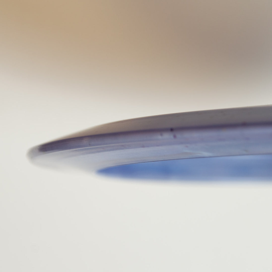 Close-up of the edge of Nina Guerrero's Aura - Diamond Metal Flake disc, highlighting its possible turnover ability against a softly blurred background.