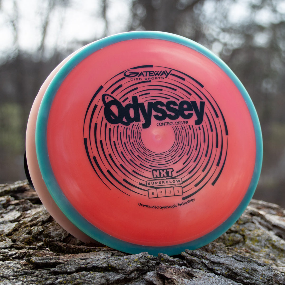 A pink and turquoise Odyssey - NXT Superglow disc golf driver stands upright on tree bark, displaying its flight numbers and other details—a striking nod to David McCormack's Odyssey Story.