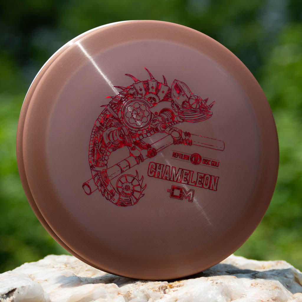 A brown Reptilian DG Chameleon — Armor fairway driver with a red mechanical Chameleon design and "Chameleon" text rests on a white rock outdoors.