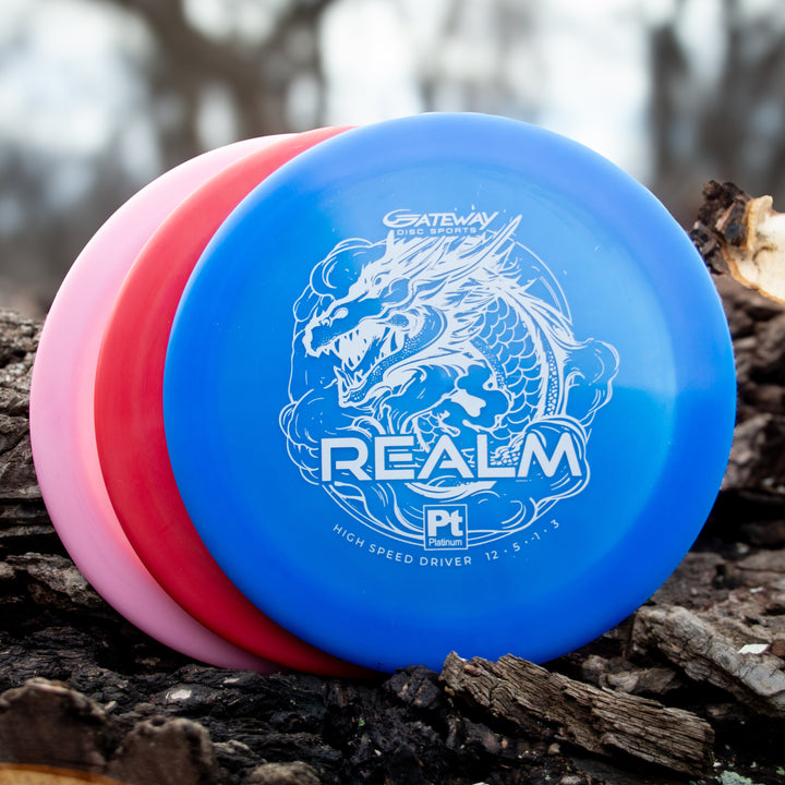 Three stacked disc golf discs rest on wood, with the top blue disc displaying a white dragon and "Realm - Platinum"€”a reliable choice for power throwers seeking top performance.
