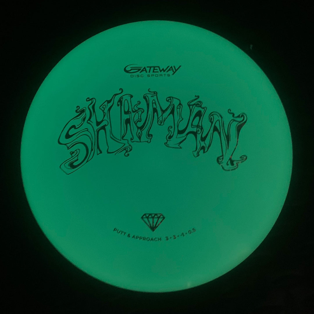 The Shaman - Diamond Superglow disc golf putter has a flat 25° nose, no bead, —SHAMAN—� and Gateway logo above specs 3-3-0-0.5 with a diamond icon—putt & approach type and features a glowing design.