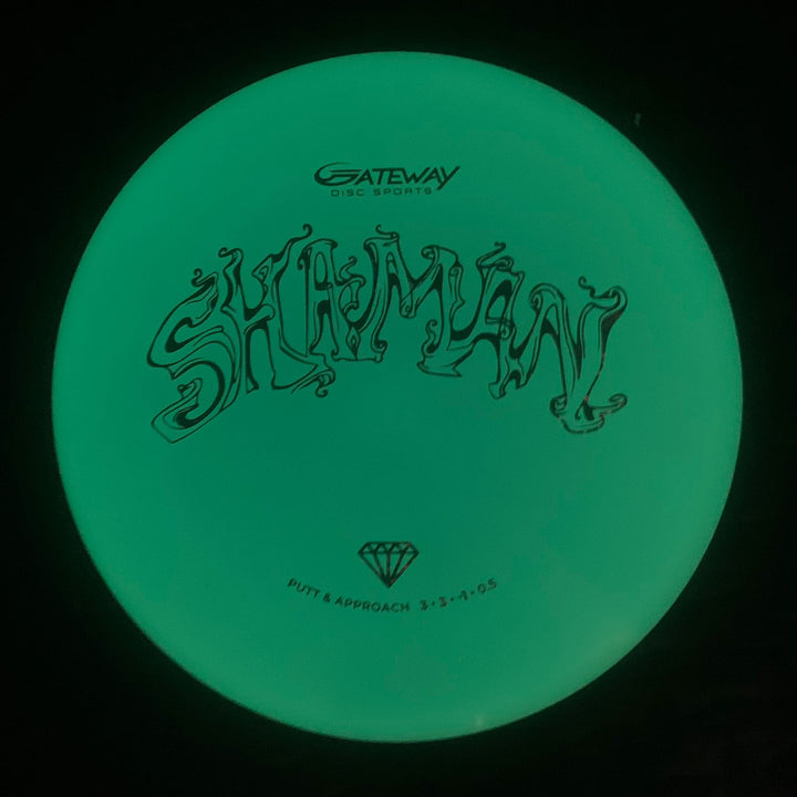 The Shaman - Diamond Superglow disc golf putter has a flat 25° nose, no bead, —SHAMAN—� and Gateway logo above specs 3-3-0-0.5 with a diamond icon—putt & approach type and features a glowing design.