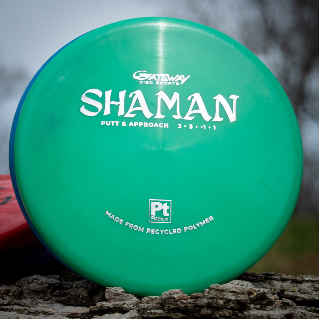 A green Gateway Shaman — Platinum disc golf putter labeled "Putt & Approach" and "Made from recycled polymer" rests outdoors—a sustainable choice crafted with recycled plastic.