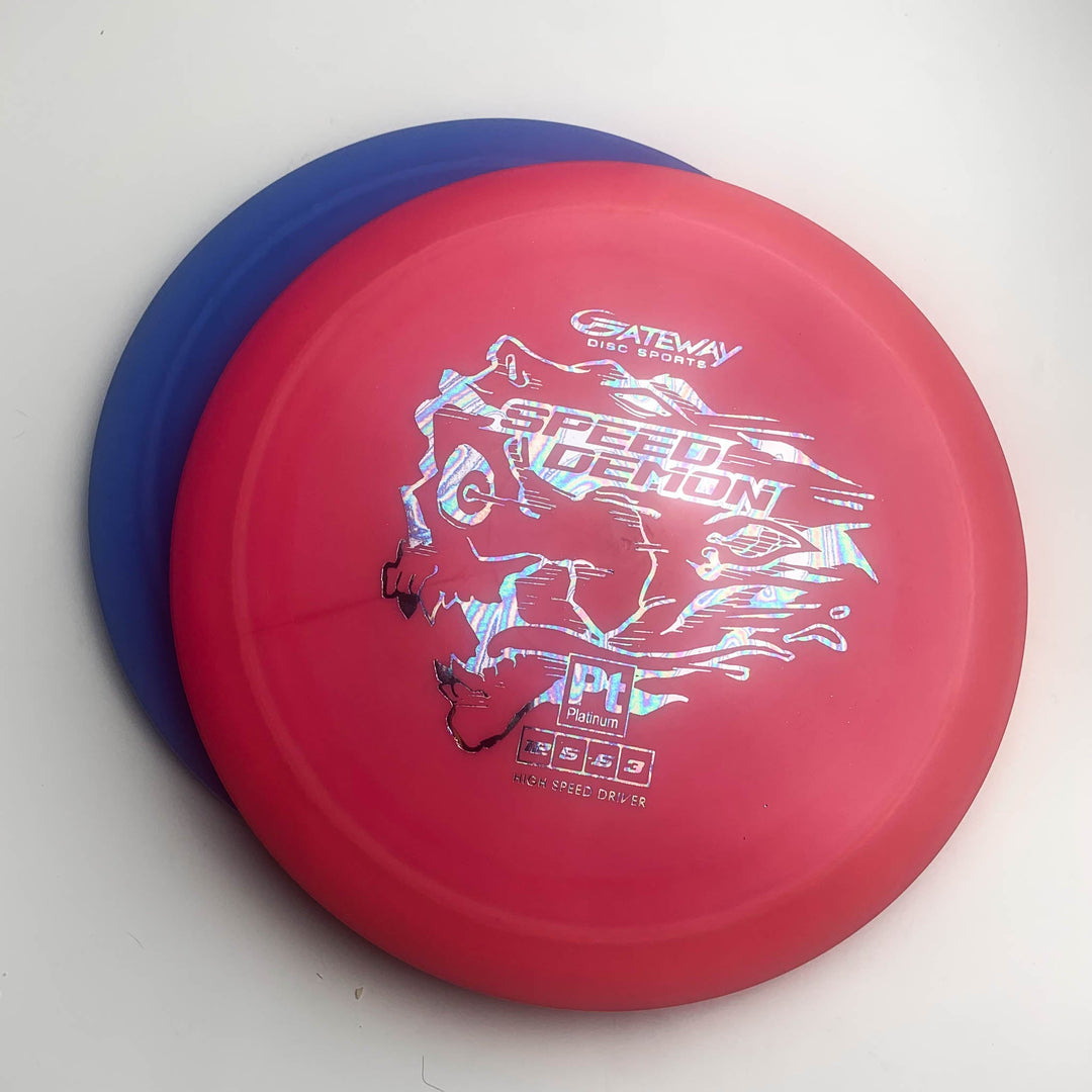 Two overlapping disc golf discs on a white surface; the top red "Speed Demon - Platinum" is an overstable distance driver ideal for power forehands, while the blue disc underneath is mostly covered.