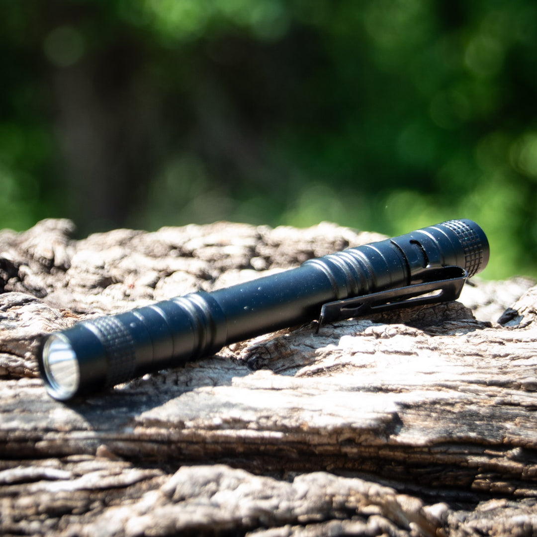 A UV Laser Pointer, shaped like a black pen, lies on textured wood with a blurred green background.