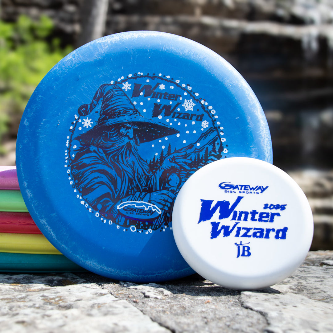 A Winter Wizard Wizard - SSSS + Mini, featuring a blue disc with wizard art and a white "Winter Wizard 2005" mini marker, sits on a rock outdoors, showcasing its classic design and max weight favored by players.
