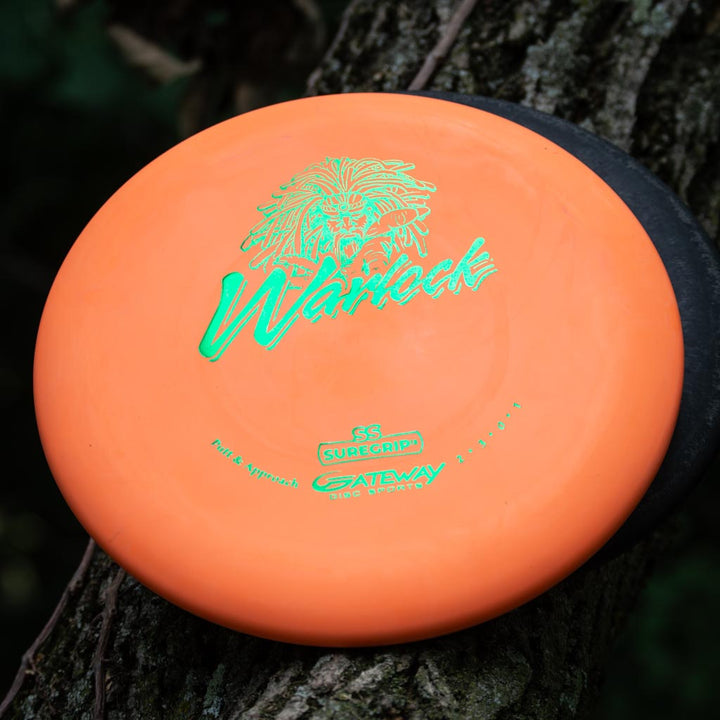 A Warlock - Suregrip - SS Super Soft beadless putter by Gateway sits on a tree trunk, with part of a black disc behind it—perfect for sharpening your approach game.